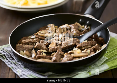 Carni bovine Stroganoff in padella, un piatto fatto di pezzi di carne di manzo, funghi e cipolla in salsa alla panna, fotografati con luce naturale Foto Stock