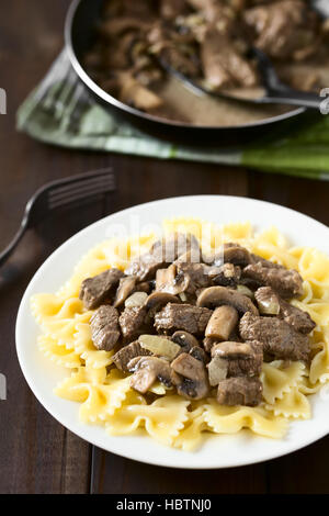 Carni bovine Stroganoff, un piatto fatto di pezzi di carne di manzo, funghi e cipolla in salsa di panna servita sulla pasta farfalle Foto Stock