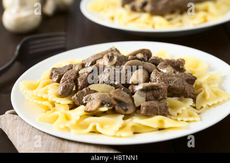 Carni bovine Stroganoff, un piatto fatto di pezzi di carne di manzo, funghi e cipolla in salsa di panna servita sulla pasta farfalle Foto Stock