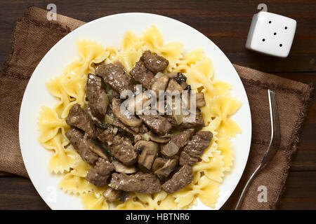 Carni bovine Stroganoff, un piatto fatto di pezzi di carne di manzo, funghi e cipolla in salsa di panna servita sulla pasta farfalle Foto Stock