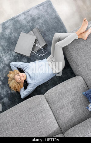 Donna sdraiata sul tappeto con le gambe sul divano. Dolorante di piedi. Rilassatevi nel comfort della vostra casa. Foto Stock
