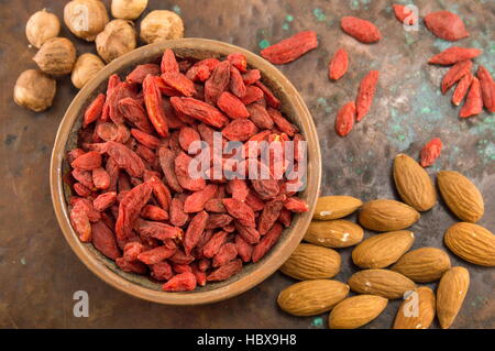 Bacche di Goji in una ciotola con le mandorle e le nocciole su sfondo rustico Foto Stock