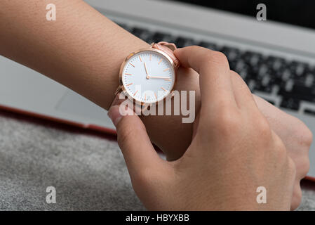 La mano della bambina con orologio da polso nella parte anteriore della scrivania con computer portatile Foto Stock