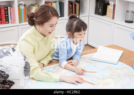 Vista laterale ritratto di sorridente madre e figlia homeschooling utilizzando una mappa Foto Stock