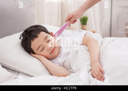 Sei-anno-vecchio ragazzo coreano dormire con una mano tenendo la sua temperatura Foto Stock