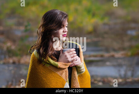 Giovane bella ragazza avvolto in una coperta e una tazza di caffè (TEA) nelle mani del all'aperto in serata d'autunno. Foto Stock