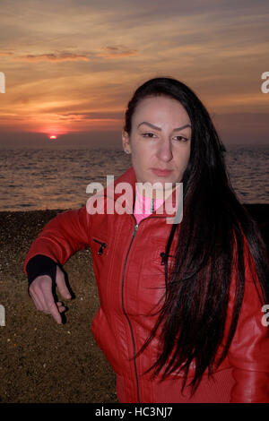 Femmina appoggiata contro un muro sul lungomare al tramonto a Southsea England Regno Unito Foto Stock