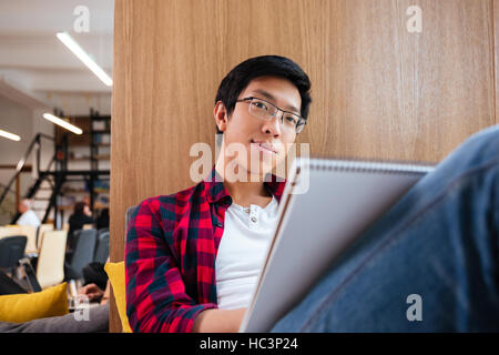 Felice asian studente studiare in biblioteca universitaria seduto sul divano. Guardando alla fotocamera. Foto Stock