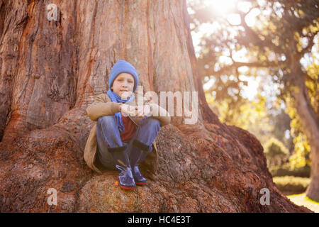 Ritratto di ragazzo abbracciando le ginocchia mentre è seduto sul tronco di albero Foto Stock