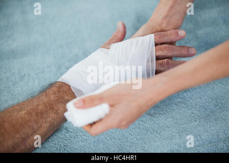 Fisioterapista mettendo fasciatura al ferito alla mano del paziente Foto Stock