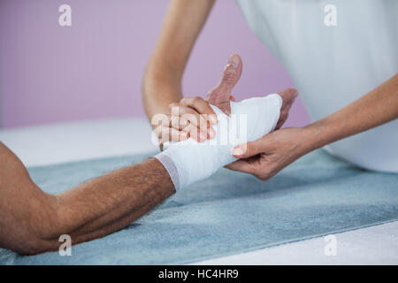 Fisioterapista mettendo fasciatura al ferito alla mano del paziente Foto Stock