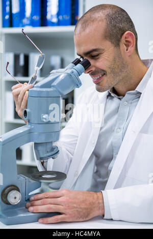 Maschio sorridente all'ottico optometrista guardando attraverso il microscopio Foto Stock