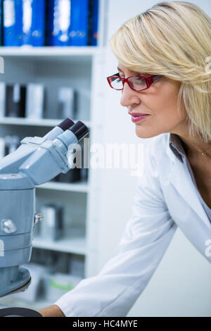 All'ottico optometrista femmina guardando attraverso il microscopio Foto Stock