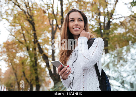 Felice affascinante giovane donna con gli auricolari per ascoltare musica dal telefono cellulare all'aperto Foto Stock