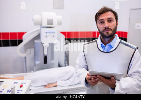 Medico tenendo tavoletta digitale e il paziente sdraiato su x ray macchina Foto Stock