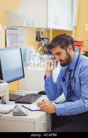 Medico seduto alla sua scrivania e parlando al telefono Foto Stock