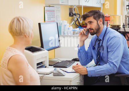 Medico seduto alla sua scrivania e parlando al telefono Foto Stock