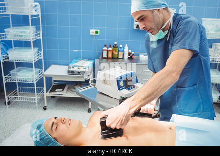 Chirurgo maschio resuscita un inconscio di un paziente con un defibrillatore Foto Stock