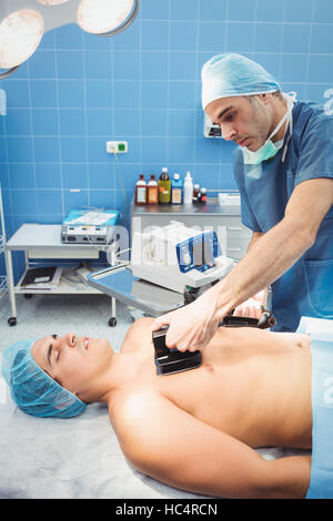 Chirurgo maschio resuscita un inconscio di un paziente con un defibrillatore Foto Stock