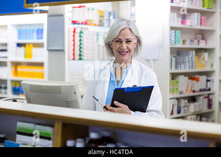 Sorridente al farmacista tenendo un blocco per appunti in farmacia Foto Stock