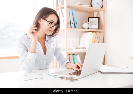 Foto di imprenditrice vestito con una camicia bianca e con gli occhiali seduto nel suo ufficio e utilizzando laptop. Foto Stock