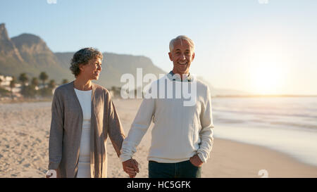 Colpo all'aperto di felice coppia matura per passeggiare sulla spiaggia. Senior uomo e donna senior facendo una passeggiata sulla riva del mare. Foto Stock