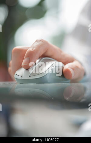 Close up di una mano di un uomo utilizzando il mouse cordless sul tavolo di vetro. Soft focus Foto Stock