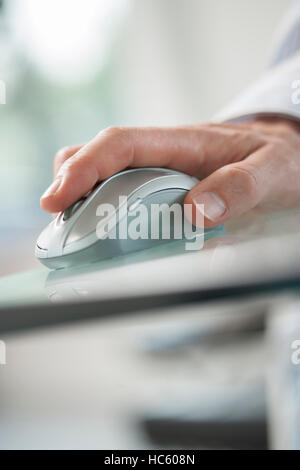 Mano di uomo con il suo indice per il comando di un mouse senza fili verde sul tavolo di vetro Foto Stock