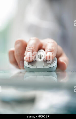 Mano d'uomo utilizzando il mouse cordless sul tavolo di vetro. Close up soft focus Foto Stock