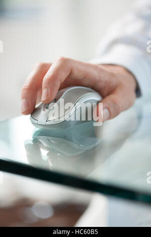 Giovane uomo la mano facendo clic su di un cordless mouse del computer su una verde tavolo in vetro Foto Stock