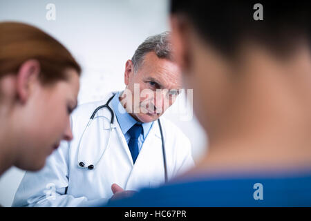 Riflessivo medico in piedi con i chirurghi in corridoio Foto Stock