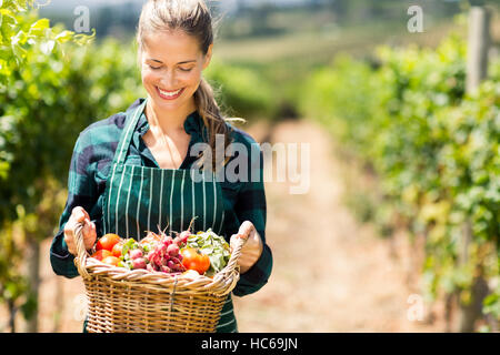 Femmina felice l'agricoltore che detiene un cesto di verdure Foto Stock