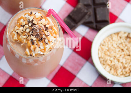 Cioccolato e burro di arachidi frullato con crema, salsa di caramello,noci tritate e scaglie di cioccolato su una coperta picnic Foto Stock