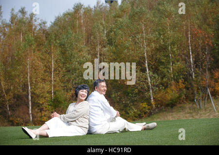 Sorridente coppia senior seduta di schiena in campo Foto Stock