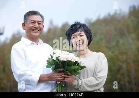 Ritratto di sorridente coppia senior tenendo un mazzo di rose all'aperto Foto Stock