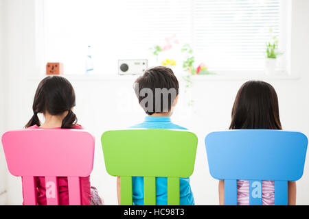Indietro di tre bambini seduti su sedie Foto Stock