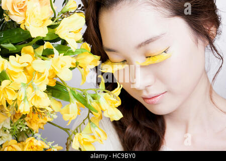 Ritratto di giovane donna coreana con giallo ciglia finte e fiori di colore giallo Foto Stock