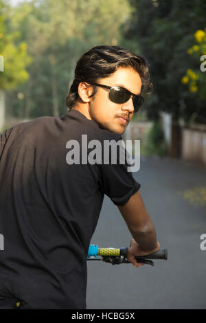 Giovane ragazzo indiano indossando occhiali da sole e in posa con noleggio biciclette Foto Stock