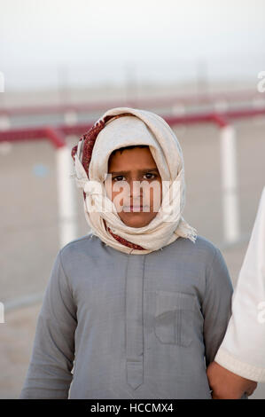 Omani ragazzo che indossa un velo sul margine di una corsa di cammelli in Oman Foto Stock