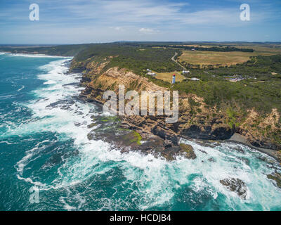 Vista aerea di Cape Schanck Lighthose e frantumazione delle onde sulla costa frastagliata in estate. Penisola di Mornington, Victoria, Australia Foto Stock