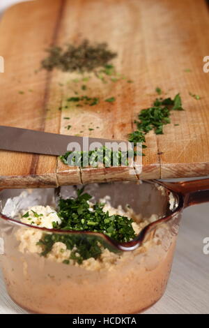 Aggiungere il prezzemolo tritato in un recipiente con riempimento. Rendendo il salmone in pasta sfoglia serie. Foto Stock