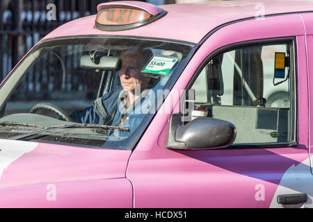 Un maschio maturo taxi driver seduta del traffico nella sua cabina rosa. Il segno legge' per noleggio' in modo che egli è in attesa per i passeggeri di grandine di lui per un viaggio. Foto Stock