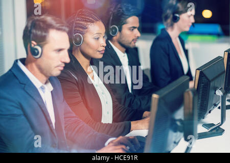 I colleghi con cuffie utilizzando il computer in ufficio Foto Stock