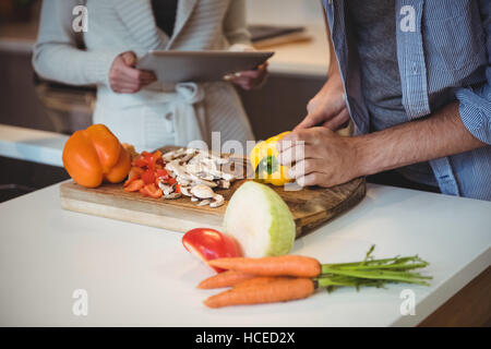 Giovane con tavoletta digitale mentre tritare verdure in cucina Foto Stock