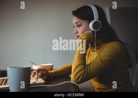 Donna ascoltando le cuffie mentre utilizzando laptop Foto Stock