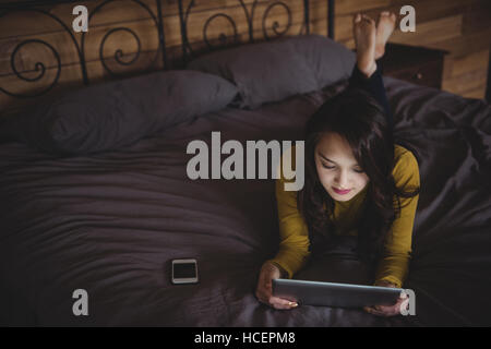 Donna sdraiata sul letto tramite digitale compressa nella camera da letto Foto Stock