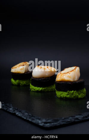 Pan-cappesante fritte servite con black pudding e frantumato purea di piselli servita su ardesia Foto Stock