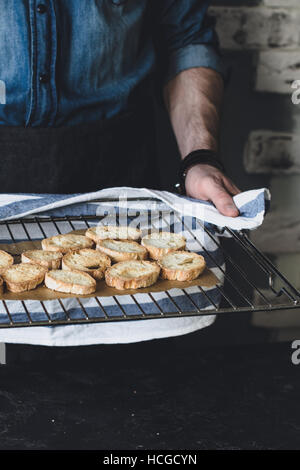 Uomo con raffreddamento per rack con dolce da forno i crostini, tagliata a fette e cotta italian baguette con olio di oliva. In verticale Foto Stock