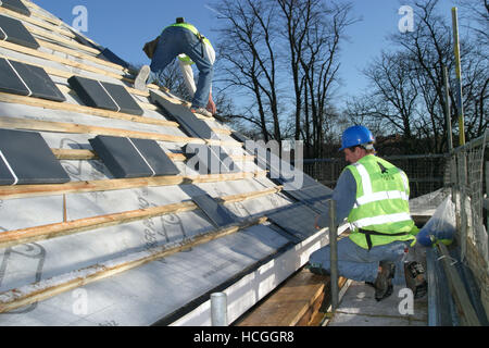 Due conciatetti attaccare piastrelle di ardesia a tetto su un alloggiamento nuovo sviluppo in Richmond, a sud di Londra, Regno Unito. Foto Stock