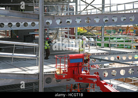 Dpi dotati lavoratore edile in cherry picker pcc montaggio prefabbricati di assi in acciaio a corona sul telaio nuovo parcheggio progetto di costruzione a Bolton Regno Unito Foto Stock